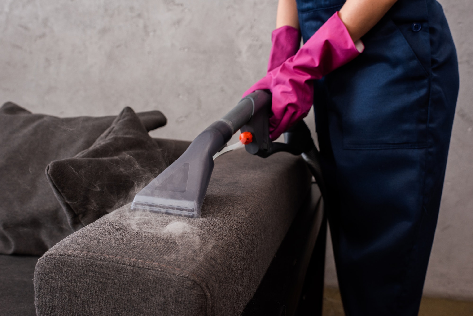 Cropped view of cleaner using vacuum cleaner with hot steam on couch upholstery